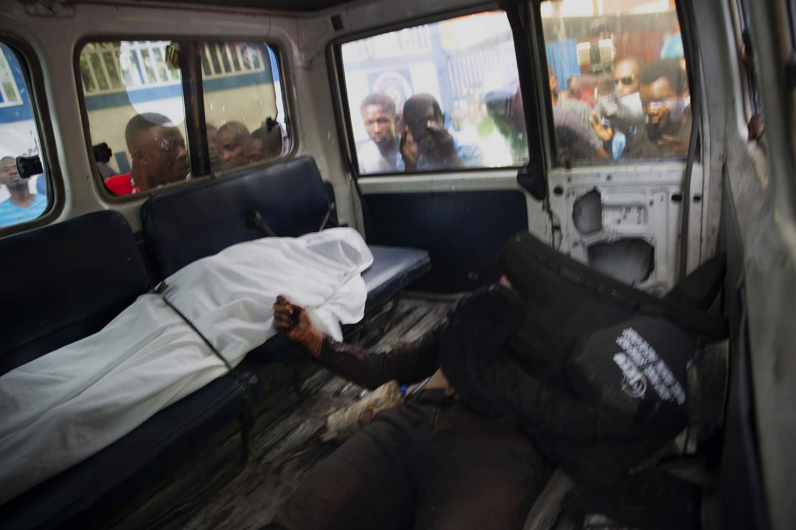 People look into the window of a police car carrying the bodies of two people killed in a shooting with police in Port-au-Prince, Haiti, Thursday, July 8, 2021. According to Police Chief Leon Charles, the two dead are suspects in the assassination of Haitian President Jovenel Mose. (AP Photo/Joseph Odelyn)