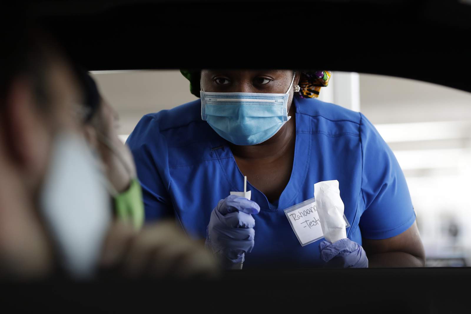 Healthcare worker Rahaana Smith instructs passengers how to use a nasal swab Friday at a drive-thru COVID-19 testing site at the Miami-Dade County Auditorium.